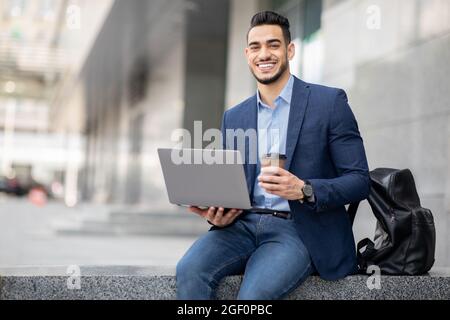 Positiver Typ aus dem Nahen Osten mit Laptop, der eine Kaffeepause im Freien hat Stockfoto
