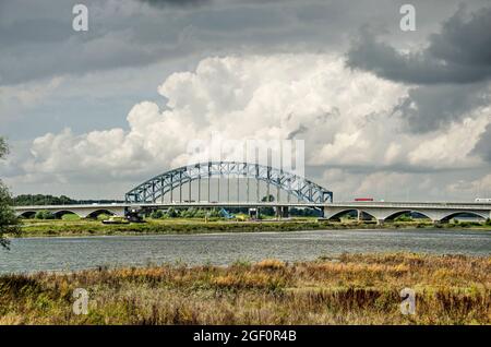 Zwolle, Niederlande, 10. August 2021: Dramatische Wolken über einer Landschaft mit dem Fluss IJssel, den Auen und der historischen Bogenbrücke Stockfoto