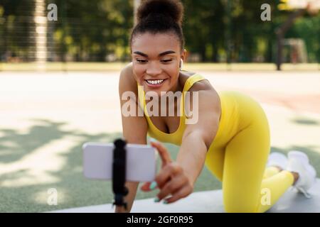 Junge schwarze Frau, die Übungen auf dem Smartphone im Freien aufzeichnet Stockfoto