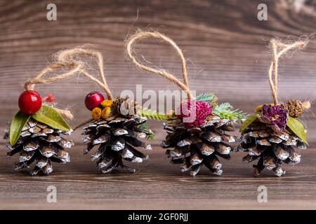 Handgemachtes Weihnachtsbaumspielzeug aus Kiefernzapfen, verziert mit natürlichen Materialien, vor dem Hintergrund eines geschnittenen Baumes. Dekorationen mit Hanf-Suspension Stockfoto