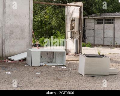 Verfallene kleine Häuser zwischen den Bäumen und der Vegetation und Dump von alten Geräten. Stockfoto