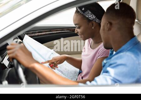 Ein glückliches schwarzes Paar, das während der Fahrt auf die Karte schaut Stockfoto