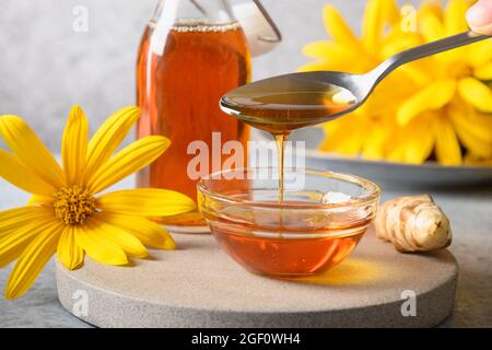 Gießen Jerusalem Artischockensirup in Schüssel, Blumen und Wurzel auf weißem Hintergrund. Nahaufnahme. Stockfoto