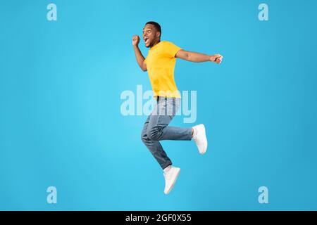 Fröhlicher Afrikanischer Mann, Der In Der Luft Springt Und Schreit, Blauer Hintergrund Stockfoto