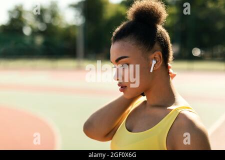 Sportliche schwarze Frau in gelber Sportkleidung, die Musik hört Stockfoto