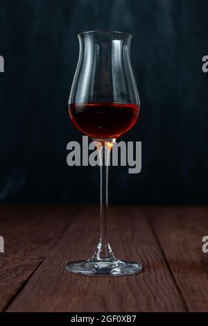 Grappa-Glas mit Brandy oder Sherry oder Calvados auf Holztisch in dunkler Stimmung. Stockfoto
