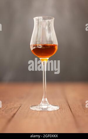 Grappa-Glas mit Brandy oder Sherry oder Calvados auf Holztisch mit hellgrauem Hintergrund. Stockfoto