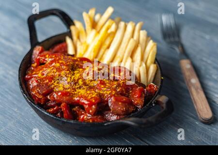 Currywurst mit pommes in schwarzer Pfanne. Stockfoto