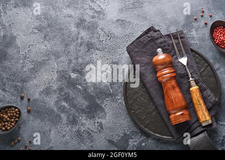 Alte Fleischgabel, schwarzer Teller, schwarzer Pfeffer und schwarzer Pfeffer und Gewürzmühle auf einem alten grauen Betongrund. Food Kochen Hintergrund und Mock up. Stockfoto