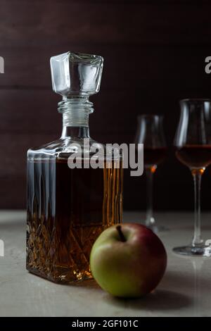 Vintage-Glas mit hausgemachten Craft Calvados mit grünem Apfel und zwei Gläsern auf Marmortisch in dunkler Stimmung. Stockfoto