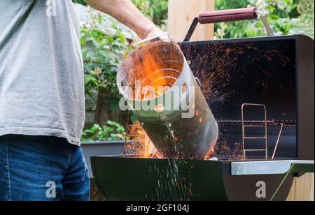 Vorbereitung des Grills mit Schornsteinstarter zum Entzünden von Holzkohle oder Briketts. Nahaufnahme von fliegenden heißen Funken. Mann, der Feuer für Gartengrill macht. Stockfoto