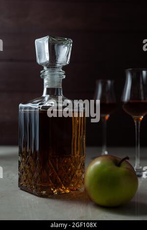 Vintage-Glas mit hausgemachten Craft Calvados mit Apfel und zwei Gläsern auf Marmortisch in dunkler Stimmung. Stockfoto