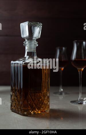 Glas mit Alkohol und zwei Gläsern. Es kann Whiskey, Cognac, Brandy, Sherry oder Calvados auf Marmortisch in dunkler Stimmung sein. Stockfoto