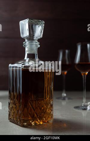 Vintage Glas mit Alkohol und zwei Gläsern. Es kann Whiskey, Cognac, Brandy, Sherry oder Calvados auf Marmor in dunkler Stimmung sein. Stockfoto