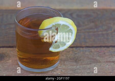 Schwarzer Tee in einem Glas mit einer Scheibe Zitrone - Konzept der Vorteile von Tee mit Zitronensaft auf Holzboden Stockfoto