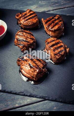 Gegrillte Schweinemedaillons mit Ketchup auf Steinplatte im rustikalen Stil. Vertikale Ausrichtung. Stockfoto