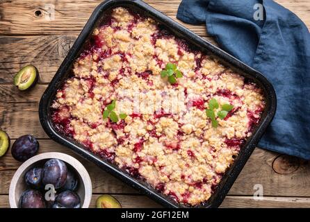 Saftige Pflaumenkuchen-Scheiben mit knuspriger Streusel-Belag auf rustikalem Holzhintergrund Stockfoto