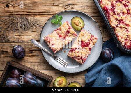 Saftige Pflaumenkuchen-Scheiben mit knuspriger Streusel-Belag auf rustikalem Holzhintergrund Stockfoto