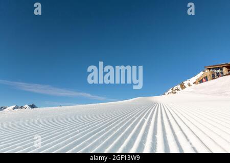 Nahaufnahme gerade Reihen von frisch präparierten Skipisten mit hell strahlender Sonne und klarem blauen Himmel Hintergrund. Schneebedeckter Berg Stockfoto