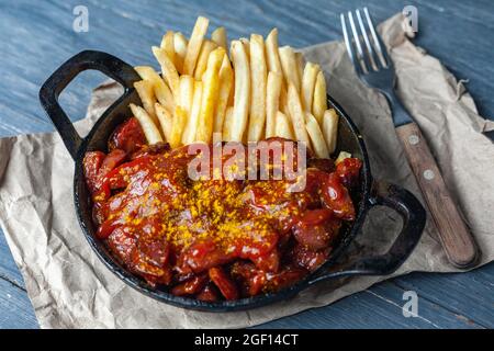 Currywurst mit pommes in schwarzer Pfanne auf Bastelpapier. Stockfoto