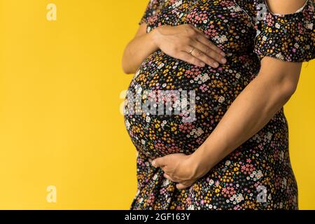 Mutterschaft, Weiblichkeit, Liebe, Fürsorge, Warten, Heißer Sommer - Helle croped Close-up unkenntlich schwanger Frau in floralen schwarzen Kleid mit Händen über Stockfoto