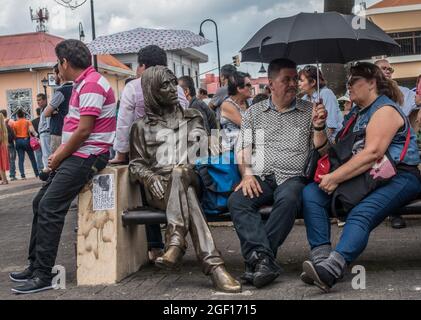 Menschen, die neben einer Bronzestatue von John Lennon in San Jose, Costa Rica, sitzen. Stockfoto