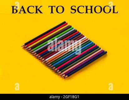 composition of wooden pencils in different colors and shades on a yellow background and the letters back to school with selective focus and copy space Stockfoto