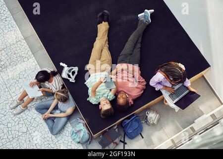 Blick von oben auf eine vielfältige Gruppe von Kindern, die sich während der Pause in der modernen Schule entspannen und Gadgets benutzen Stockfoto