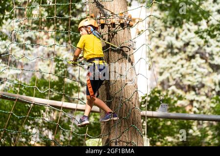 Teenager-Mädchen geht auf Scharnierweg in extreme Seil Park im Sommerwald. Höhenklettertraining des Kindes auf Abenteuerstrecke, ausgestattet mit Stockfoto