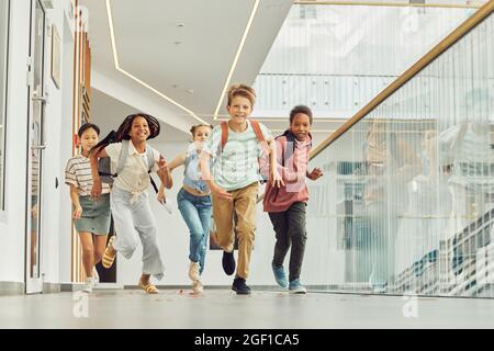 Porträt einer multiethnischen Gruppe von Schulkindern, die in Innenräumen auf die Kamera zulaufen und fröhlich lächeln, Platz zum Kopieren Stockfoto