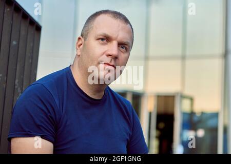 Kaukasischer Mann mittleren Alters sitzt in der Nähe des Bürogebäudes. Stockfoto