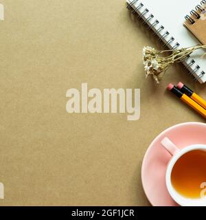 Notizbuch, Bleistift, trockene Blume, Teetasse auf braunem Hintergrund. Flach liegend, Draufsicht, Kopierraum. Arbeits- und Studienort Stockfoto