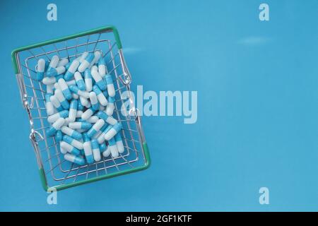 Pillen in einem Lebensmittelkorb. Medikamentenkapseln auf dem Tisch. Käufer in der Apotheke. Medikamente online bestellen. Pillen auf blauem Hintergrund in einer Schachtel. Stockfoto