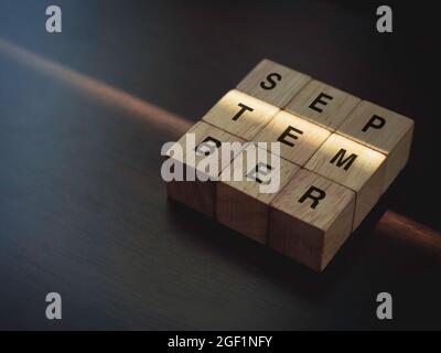 September, Worte auf hölzernen Würfelblöcken auf dunkelbraunem Holzhintergrund mit Kopierraum. Stockfoto