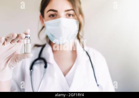 Ärztin oder Krankenschwester in Uniform, Handschuhe, Gesichtsmaske mit Impfstoffflasche Stockfoto