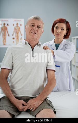 Physiotherapeutin, die einen älteren Patienten untersucht, massiert verschiedene Triggerpunkte auf seinem Rücken und askiert, wenn es schmerzhaft ist Stockfoto