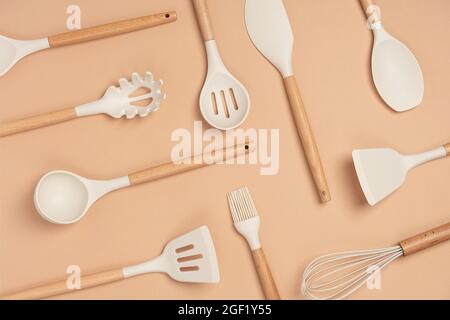 Muster aus Kochgeschirr-Set. Küchengeräte aus Silikon mit Holzgriff auf beigem Hintergrund. Draufsicht Flat Lay. Stockfoto