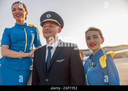 Porträt eines Piloten mit Hut, der zusammen mit zwei Lufthostessen in blauer Uniform im Freien posiert Stockfoto