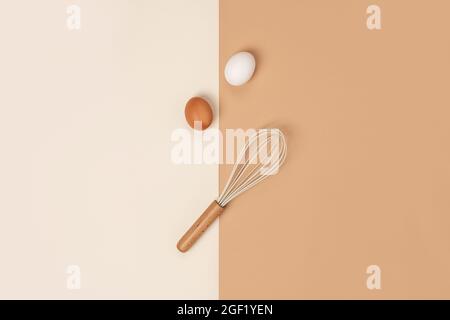 Zwei braune Eier und Schneebesen mit Holzgriff auf beigem Hintergrund. Flat Lay Draufsicht Konzept. Stockfoto