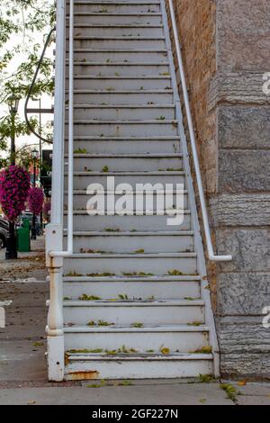 Alte, verwitterte, weiß gestrichene Holztreppe entlang eines attraktiven Steingebäudes in einem städtischen Gehsteig mit hellem Schatten Stockfoto