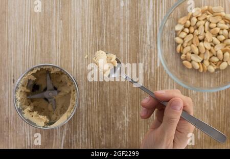 Draufsicht auf Frau Hand halten Löffel mit hausgemachter Erdnussbutter in Mühle auf Holz Hintergrund gemacht Stockfoto