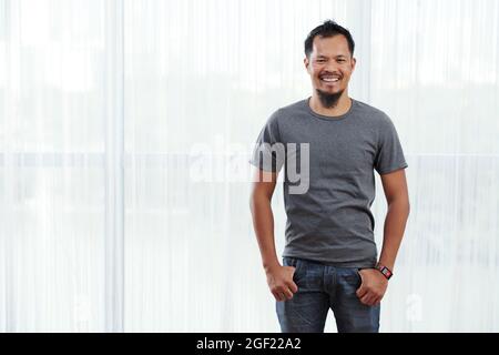 Porträt eines fröhlichen jungen Mannes, der mit Händen in Taschen wie Jeans steht Stockfoto