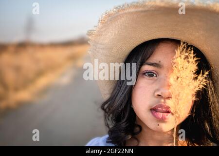 Ein junges indisches Mädchen in einem trockenen Feld, das einen Strohhut trägt Stockfoto