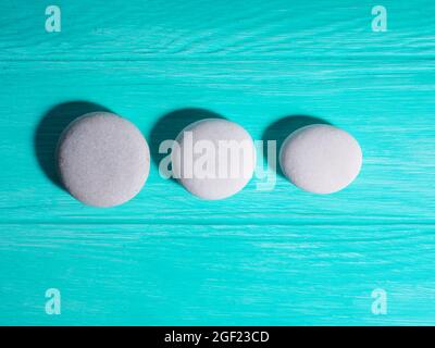 Drei weiße Zen-Steine in einer Reihe in einer Linie auf blauem Hintergrund. Stockfoto