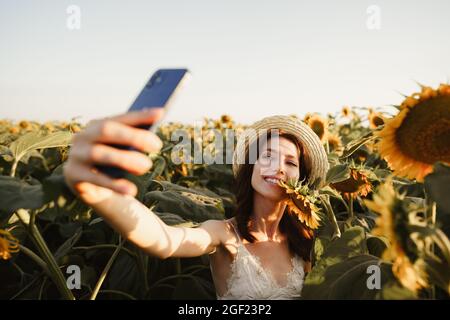 Junge lächelnde Frau im Hut, die Selfie-Foto im Sonnenblumenfeld Stockfoto