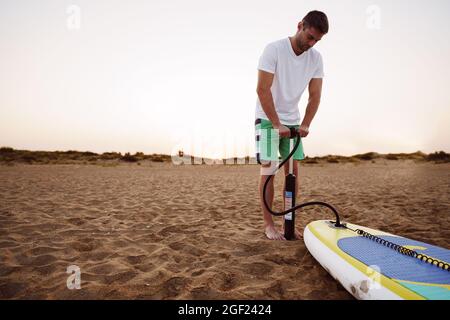 Junger Mann, der bei Sonnenaufgang am Strand Paddel aufbläht Stockfoto