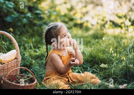 Mädchen im Overall, sitzt auf dem Gras und isst Himbeeren Stockfoto