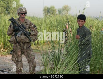 SPC der US-Armee. Michael Mizer, ein Sanitäter der Bravo-Truppe, der 4. Staffel, des 9. Kavallerieregiments, des 2. Panzerbrigade-Kampfteams, der 1. Kavalleriedivision, zugewiesen wurde, posiert für ein Foto mit einem lokalen afghanischen Jungen während einer Anwesenheitspatrouille um die Vorwärtsoperationsbasis Fenty in der Provinz Nangarhar, Afghanistan, 22. August 2013 Der Zweck der morgendlichen Patrouille war es, die Sicherheit von Fentys Umkreis zu überprüfen und die lokale Bevölkerung zu engagieren. (USA Foto der Armee-Nationalgarde von Sgt. Margaret Taylor/Freigegeben) Stockfoto