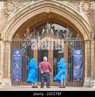 Ein englischer Priester und zwei afrikanische Nonnen am Eingang der christlichen mittelalterlichen Kirche St. Peter in Peterborough, England. Stockfoto