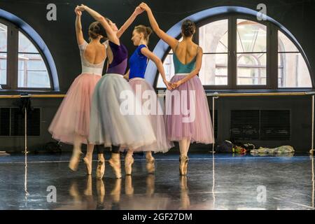 Vier junge Balletttänzerinnen, die in farbenfrohen Tutus gekleidet sind, Proben für eine Aufführung in einem Proberaum Stockfoto